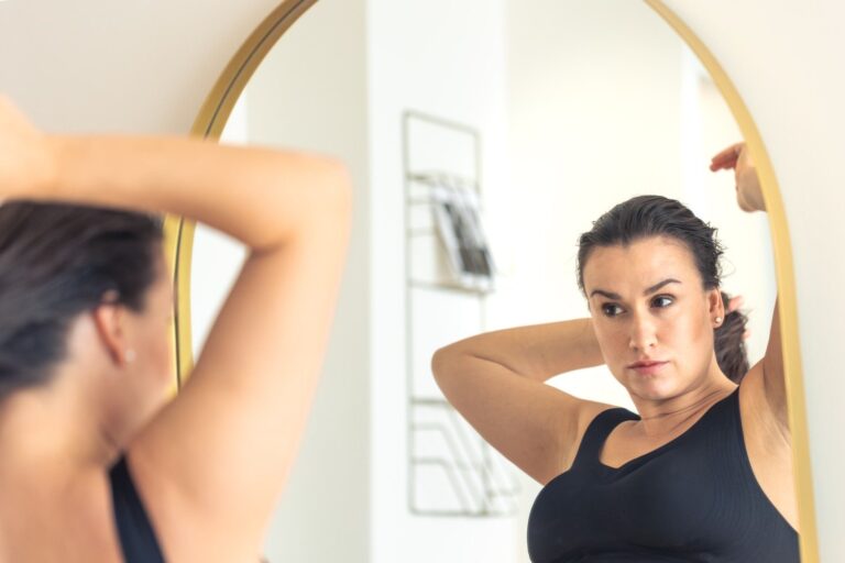 Woman checking armpit fat and underarm area in mirror